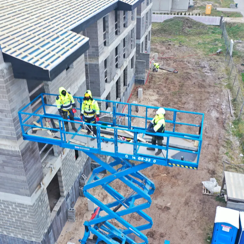 Jumtu meistari uz pacēlāja pie daudzstāvu ēkas jumta