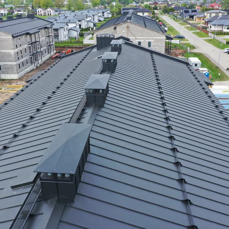 Daudzdzīvokļu ēkas tumšais metāla jumts ar ventilācijas izvadiem
