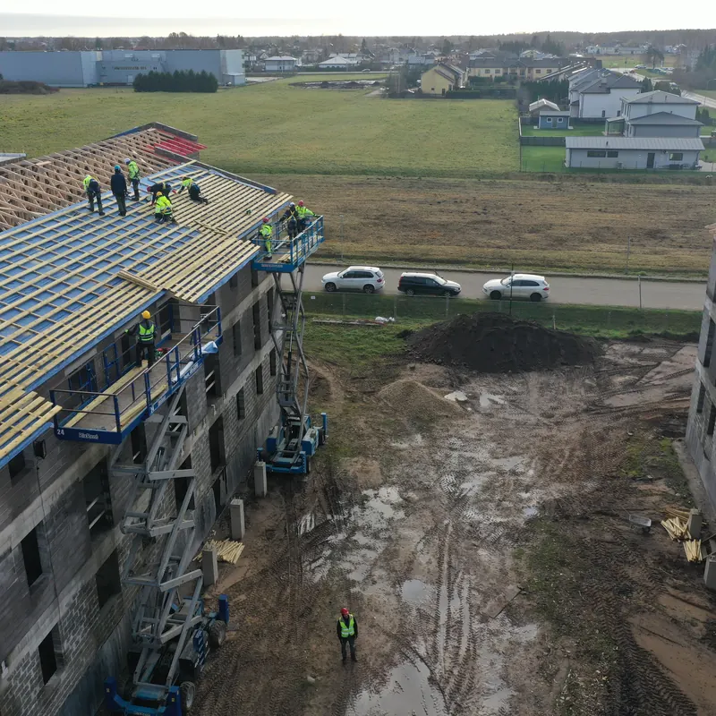 Strādnieki uz daudzdzīvokļu mājas jumta konstrukcijas