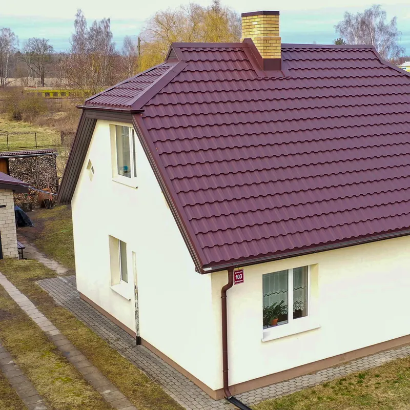 Tumši sarkans metāldakstiņu jumts baltai privātmājai
